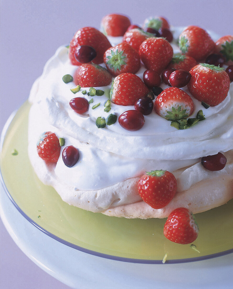 Baisertorte mit Erdbeeren, halben Kirschen und gehackten Pistazien