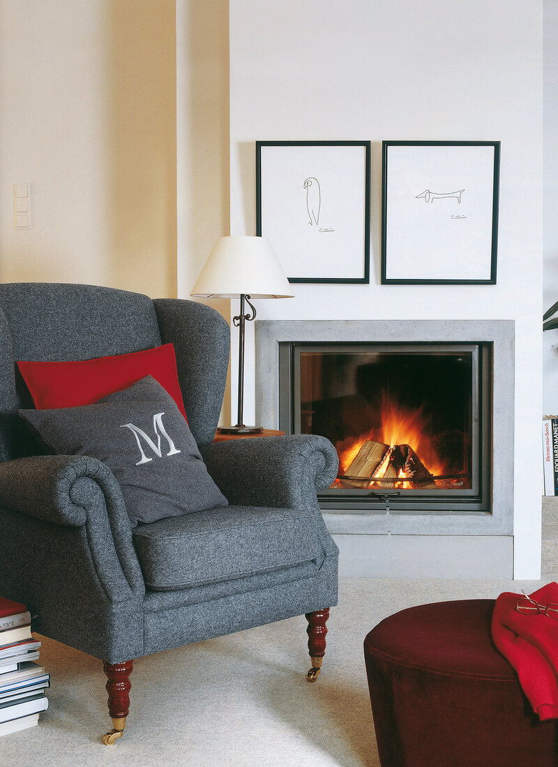 Gray wingback chair before and red foot stool burning fireplace