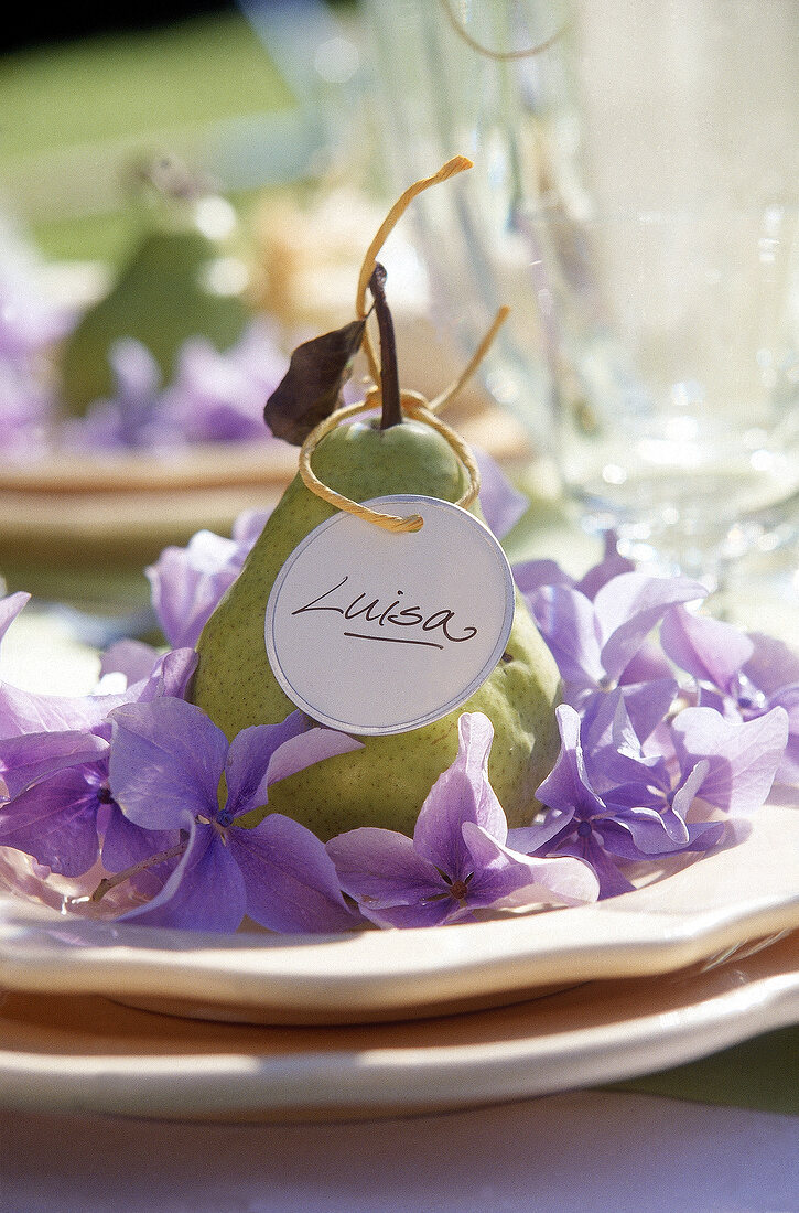 A pear as edible place card, decorated with purple hydrangea blossoms