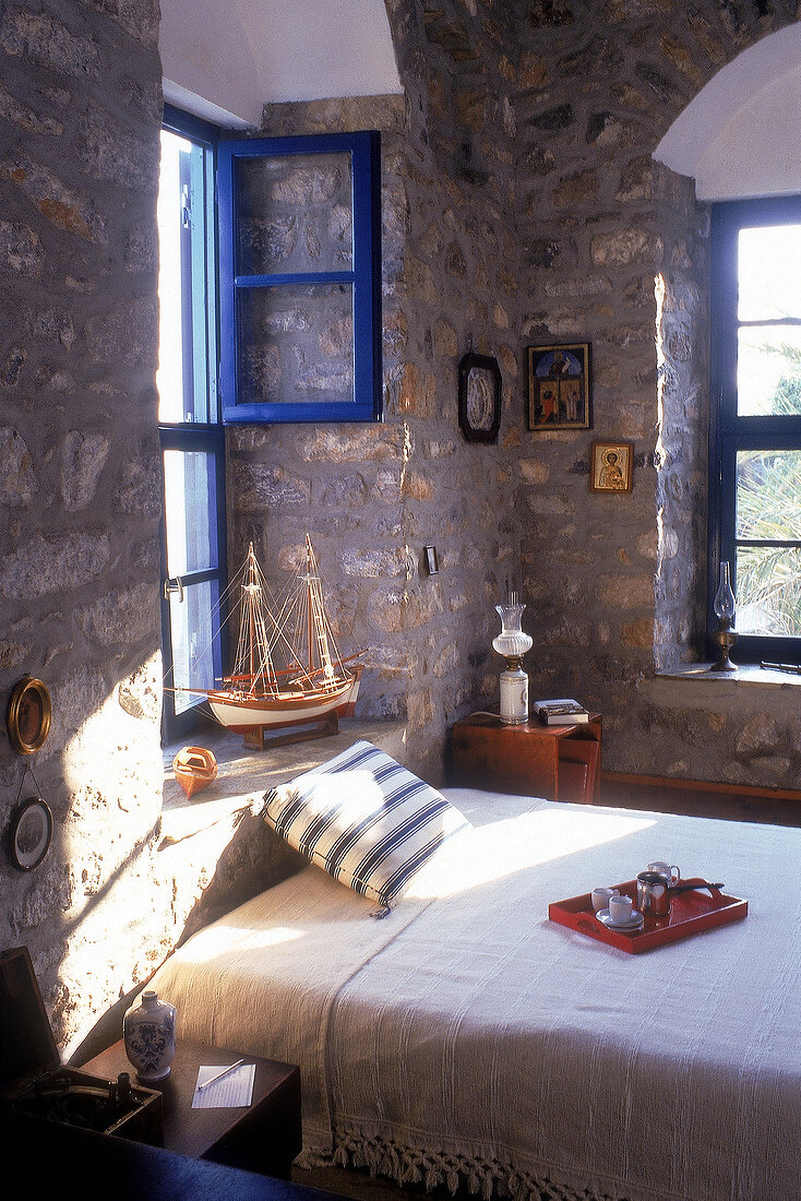 Doppelbett mit weißer Überdecke in schattigem Zimmer mit Steinmauern