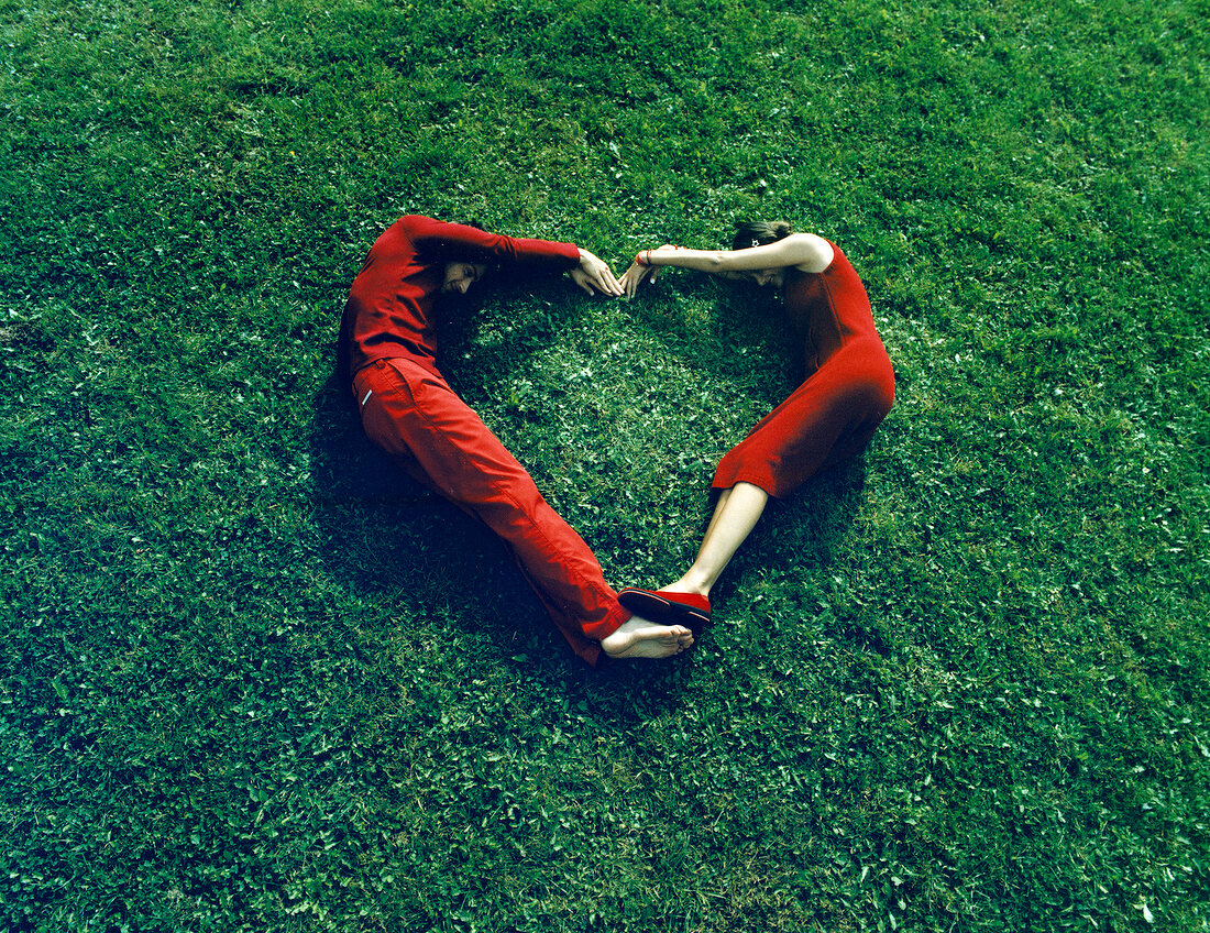 Ansicht von Oben: Paar in rot liegt auf Wiese, bilden ein Herz m. Körper