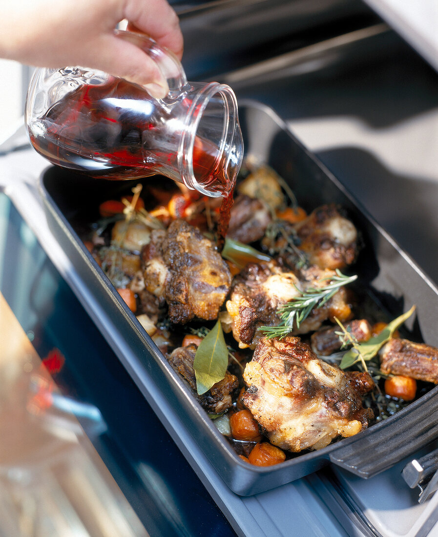 Close-up of oxtail in roasting dish being topped with red wine