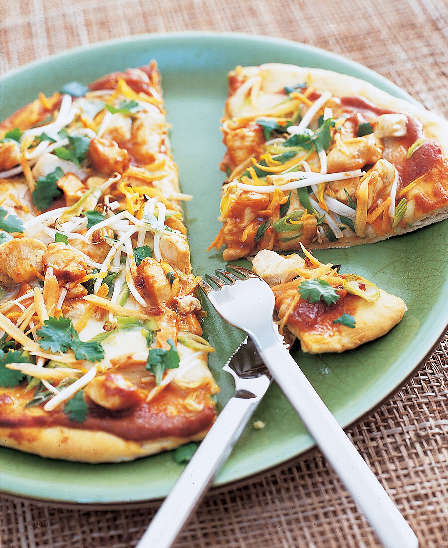 Eine Pizza mit Hähnchen und Sprossen in mehreren Teilen auf einem Teller