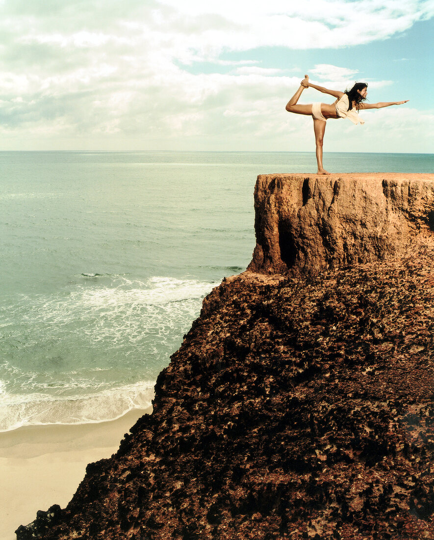Young woman performing stretching exercise on cliff near sea