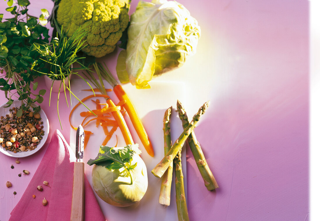 Kohlrabi, sprouts, carrot strips, green asparagus and herbs kept on pink surface