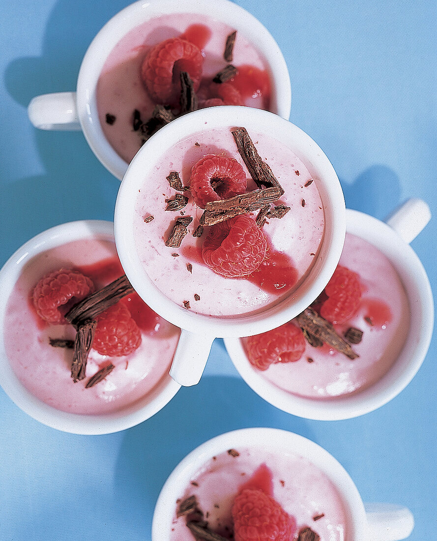 Mehrere Tassen mit Himbeermousse, garniert mit Himbeeren