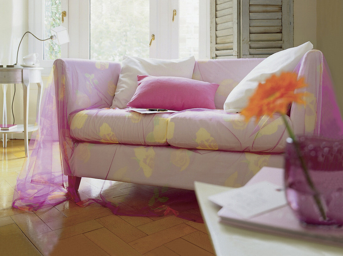 Helles Sofa mit transparentem Überwurf aus rosa Stoff, große Kissen