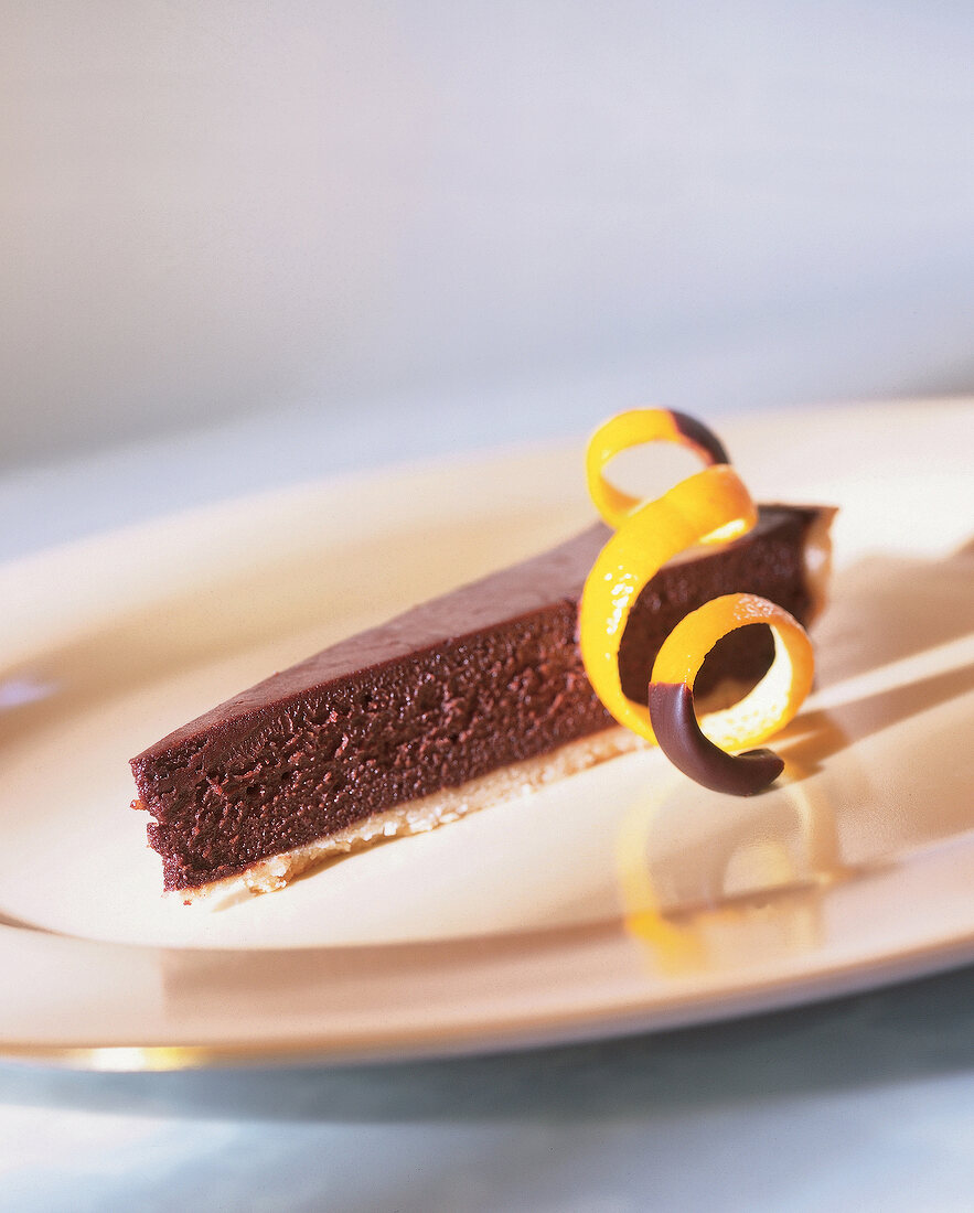 Piece of chocolate tart with candied orange peel on plate