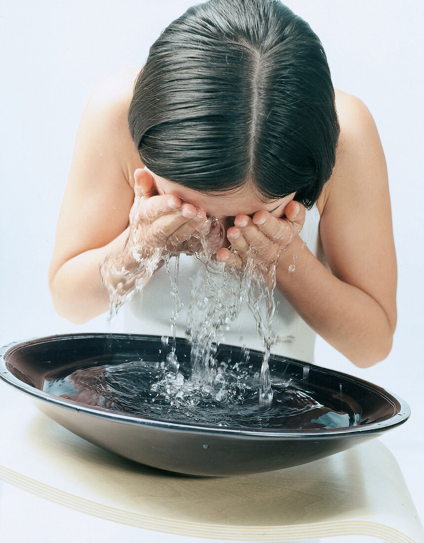 Dunkelhaarige Frau spritzt Wasser aus einer Schale ins Gesicht