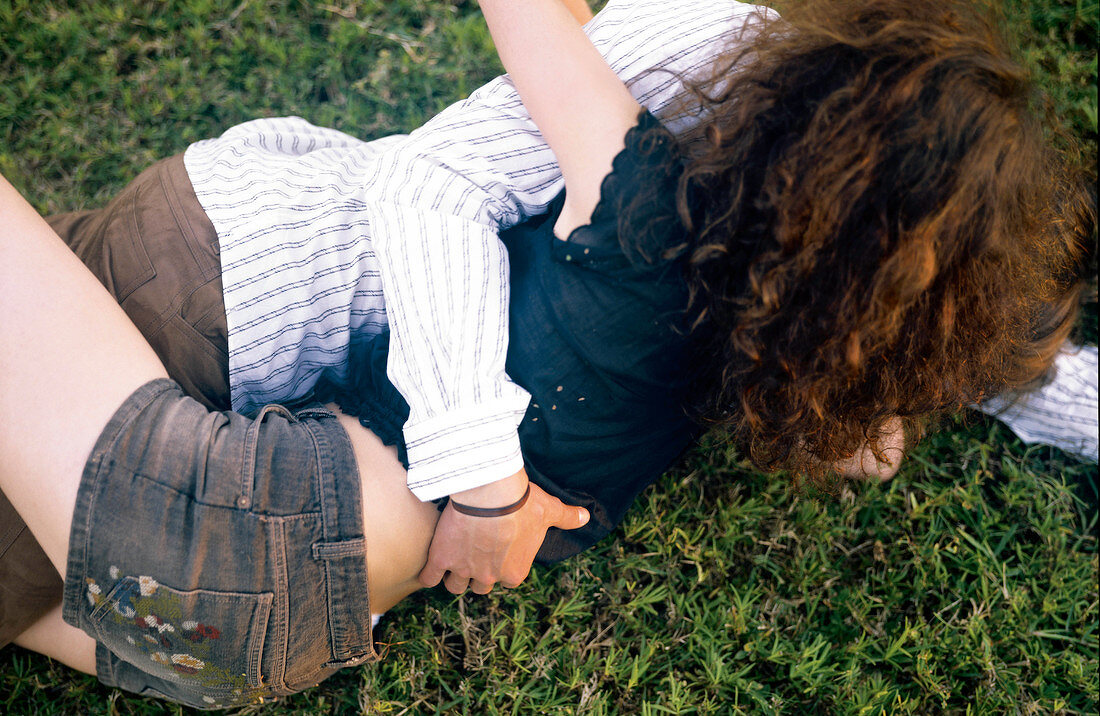 Loving young couple cuddling each other while lying on grass with arms around each other