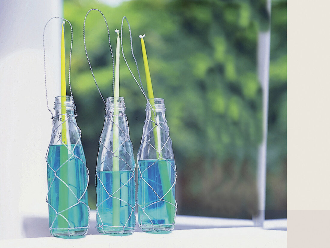 Stabkerzen in Flaschen mit türkis ge -färbtem Wasser + Drahthalterung