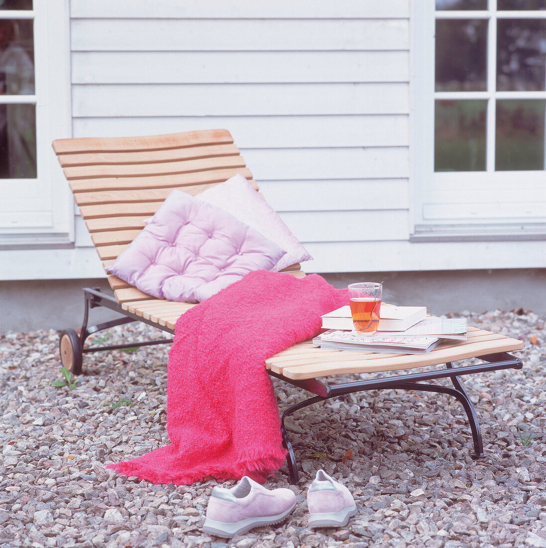 Pink blanket, pillow and sneakers on metal framed wooden deck chair