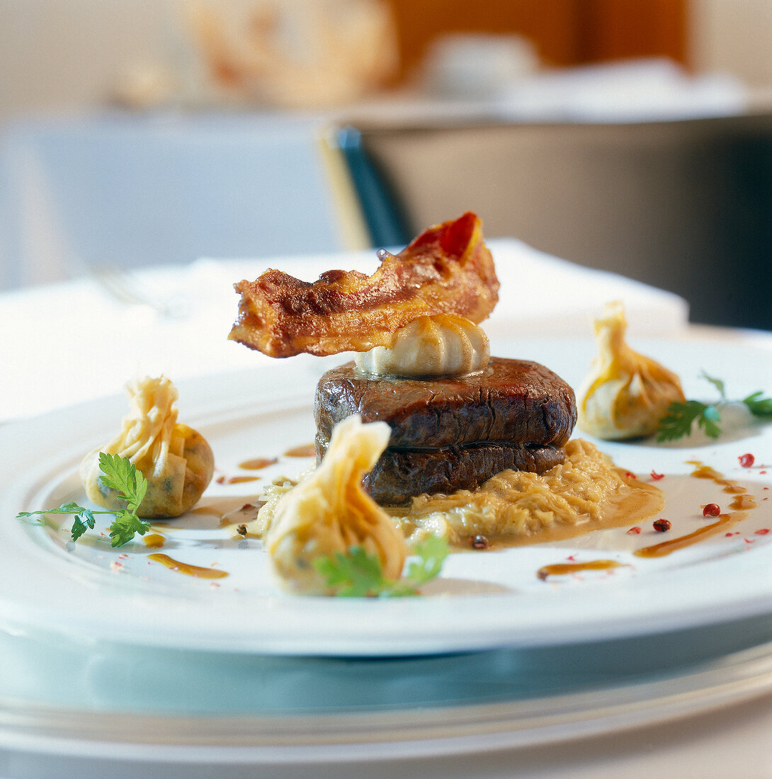 Close-up of bull fillet on sauerkraut with potato sacks and bacon on plate