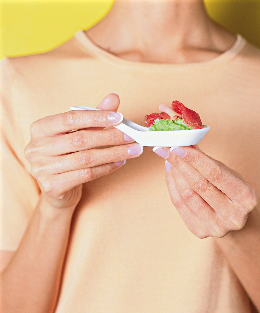 Close-up of woman holding marinated tuna with wasabi potato puree in ceramic spoon