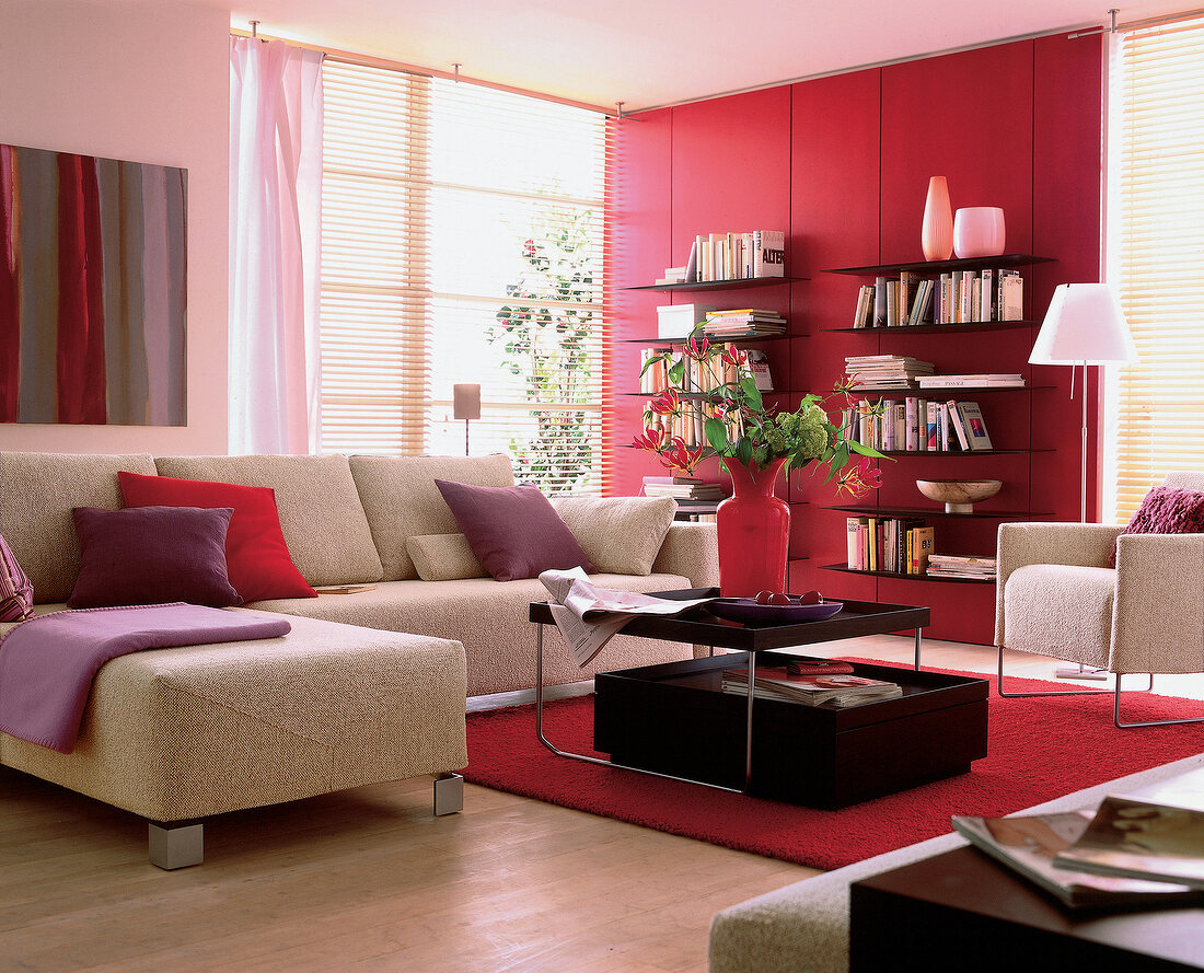 Helles Sofa mit Couchtisch auf rotem Teppich.Bücherrregal vor roter Wand