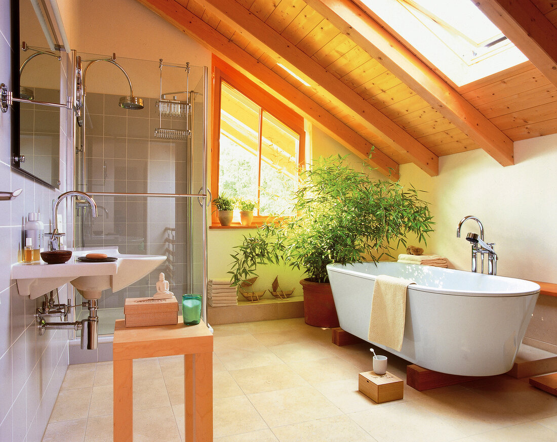 Interior of bathroom with wooden roof, white bathtub and shower enclosure