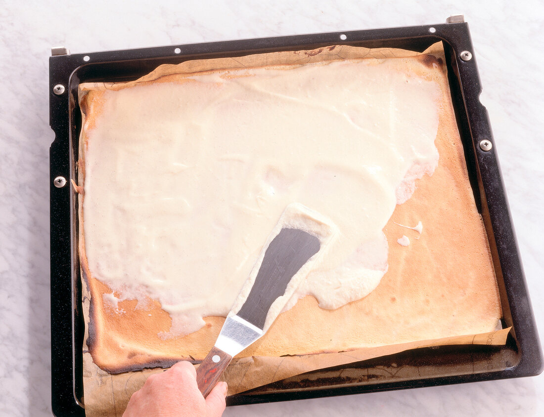 Spreading cream on layer of cake in baking tray