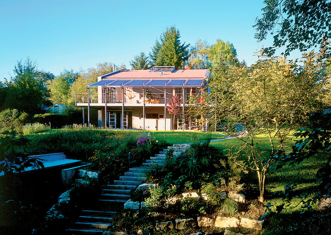 Blick aus dem Garten auf ein Wohnhaus, blaue Markisen