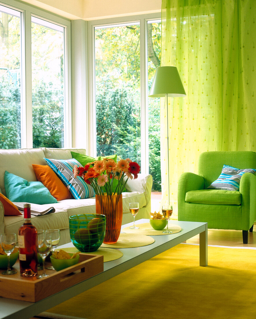 Colourful living room with chair sofa, coloured cushions, green curtains and lamp
