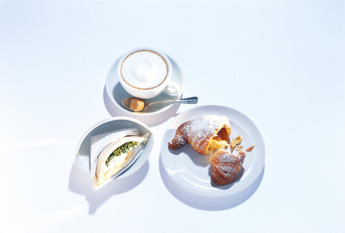 Breakfast table set with cornetto, tramezzino and cappuccino on plate