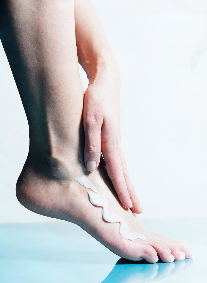 Close-up of woman's hand applying cream on foot for foot care against white background