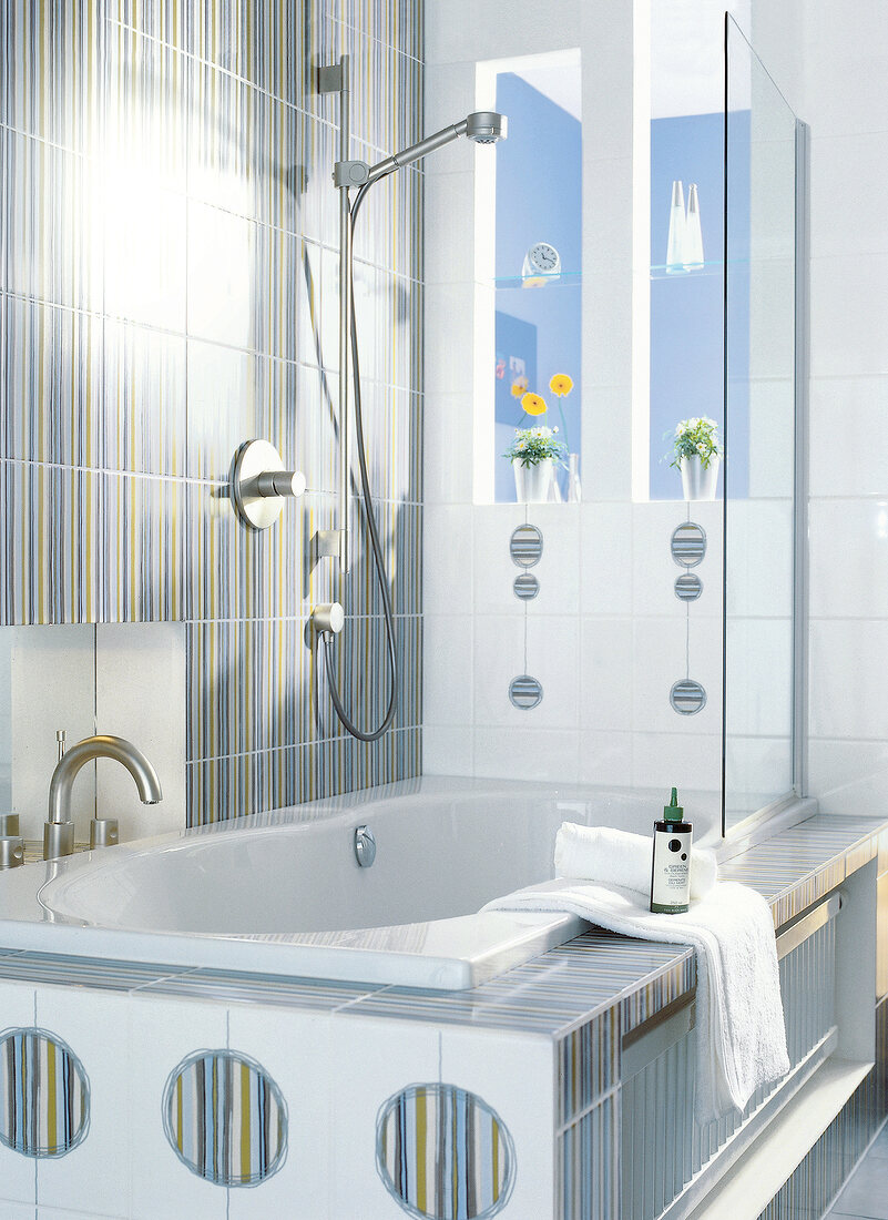 Striped tiles and bathtub with glass dividing wall in bathroom