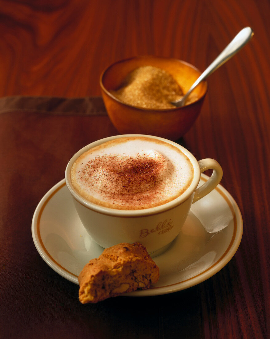 Cappuccino in white cup with a piece of cookie on saucer on wooden surface