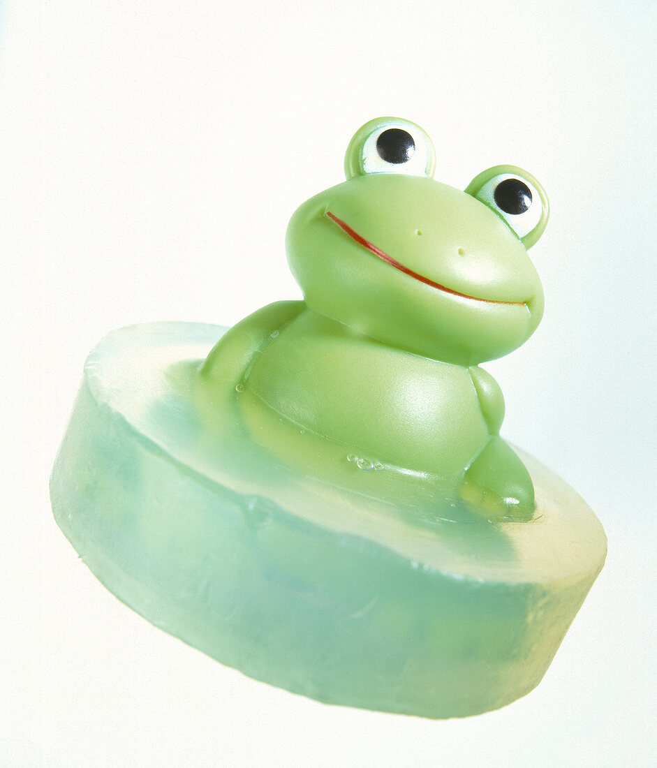 Close-up of green soap with plastic frog on white background