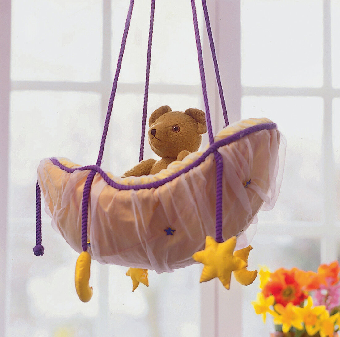 Teddybär sitzt in einer Schaukel an der gelbe Sterne und ein Mond hängen
