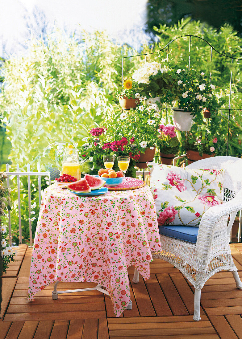 Gedeckter Tisch und weißer Korbstuhl auf einem Balkon mit Topfpflanzen