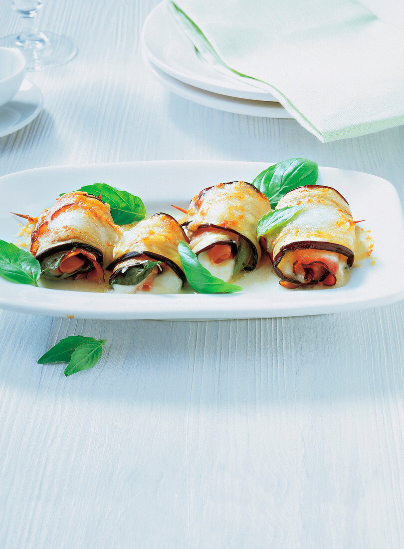 Four eggplant rolls with mint leaves served on dish