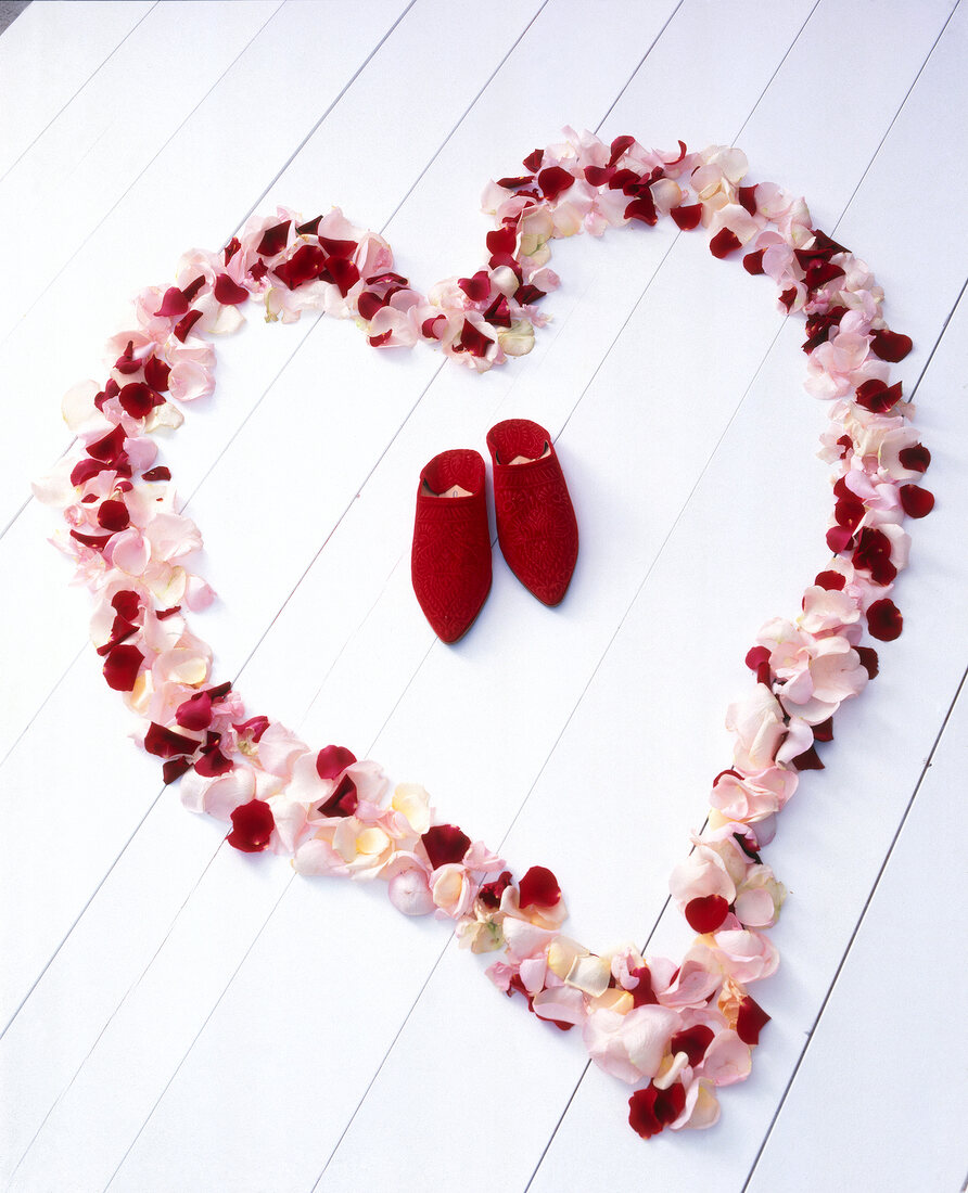 Big heart made of petals with pair of red shoes in middle on wooden surface