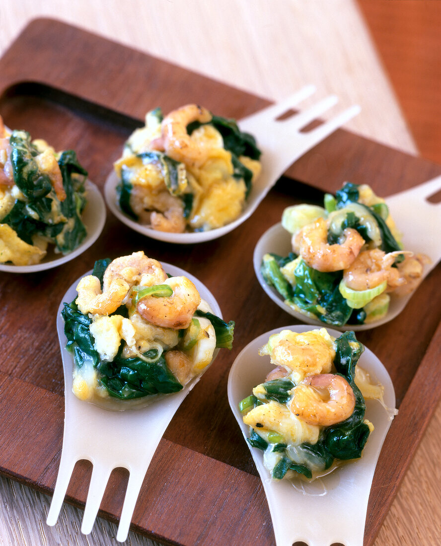 Spoon food with spinach, crabs and scrambled eggs on wooden platter