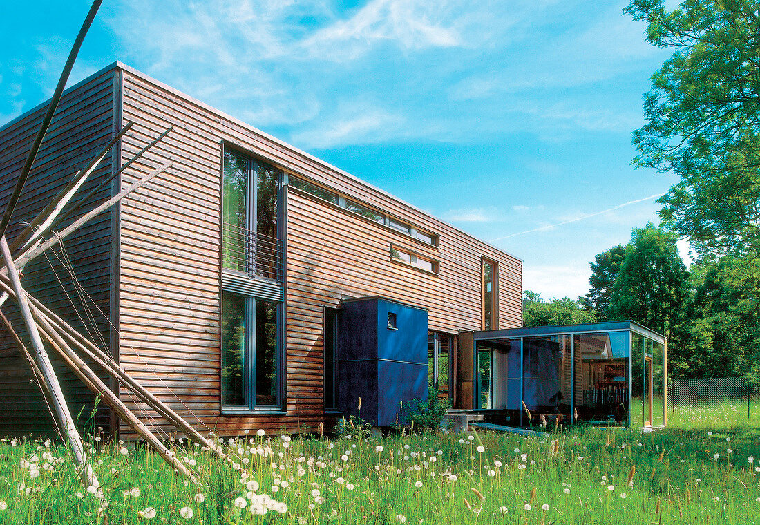 modernes Holzhaus auf Pfeilern mit Glasanbau im Grünen