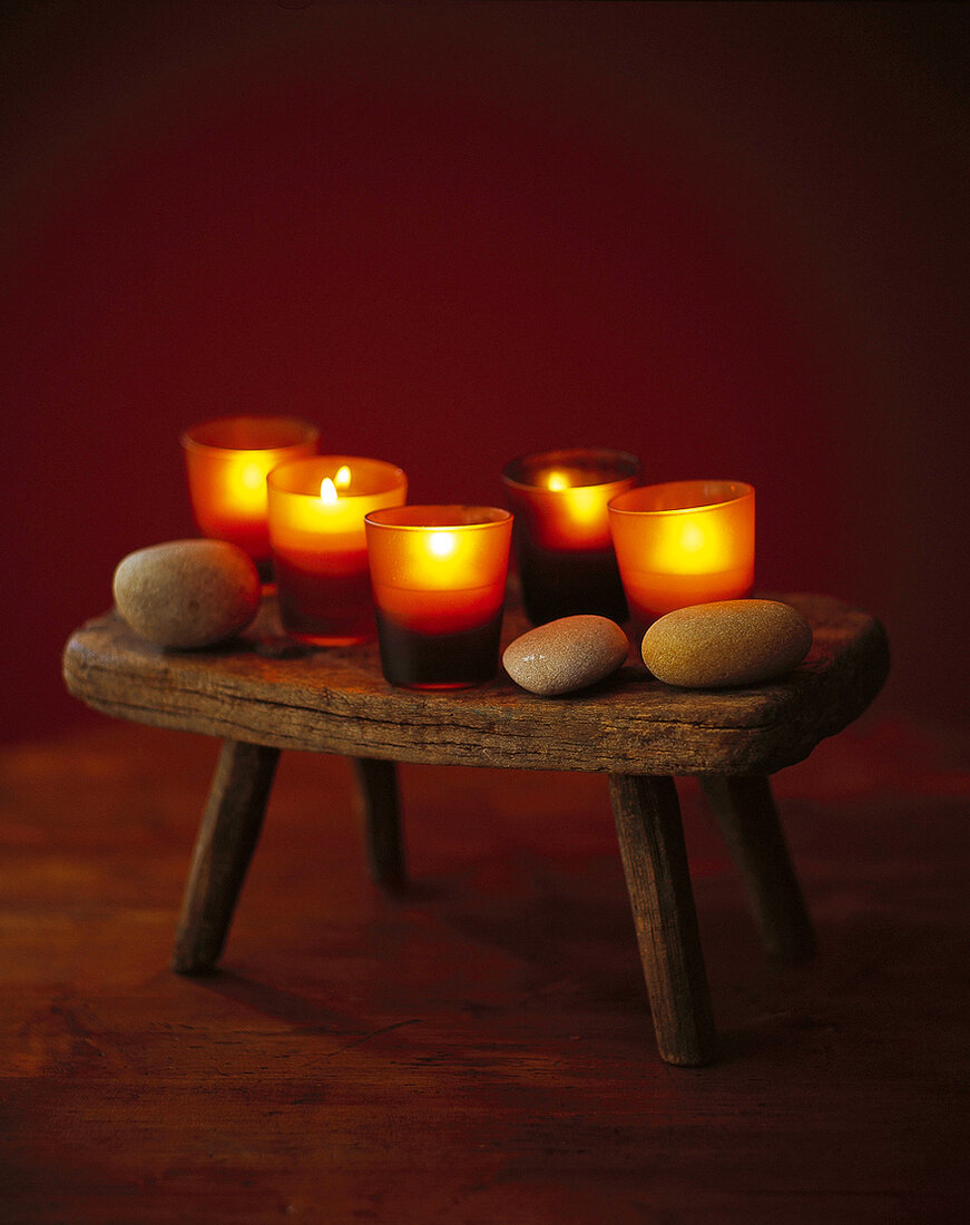 Alter Holzschemel mit brennenden Kerzen, Schwimmkerzen in Gläsern