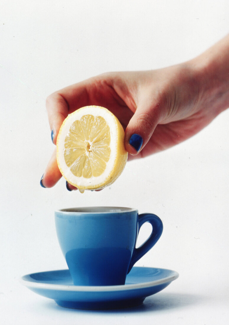 Zitrone wird über einer blauen Kaffeetasse ausgepresst, Studio