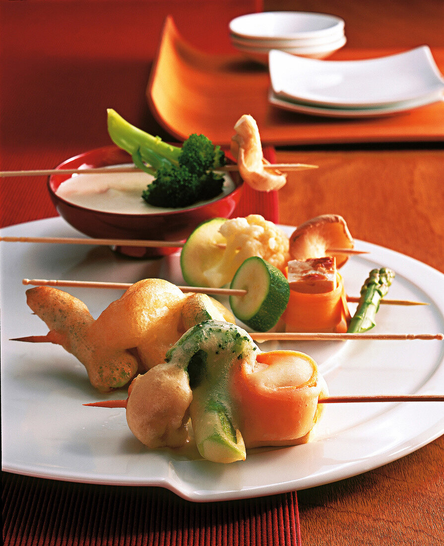 Vegetables, mushrooms and tofu in batter stuck on skewers for preparing tempura