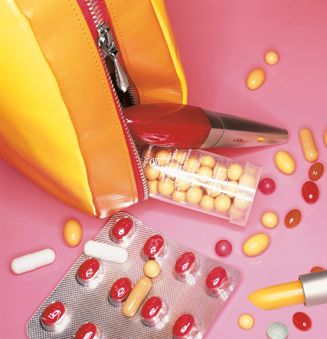 Close-up of medicinal pills scattered near make up bag and lipstick on a pink background