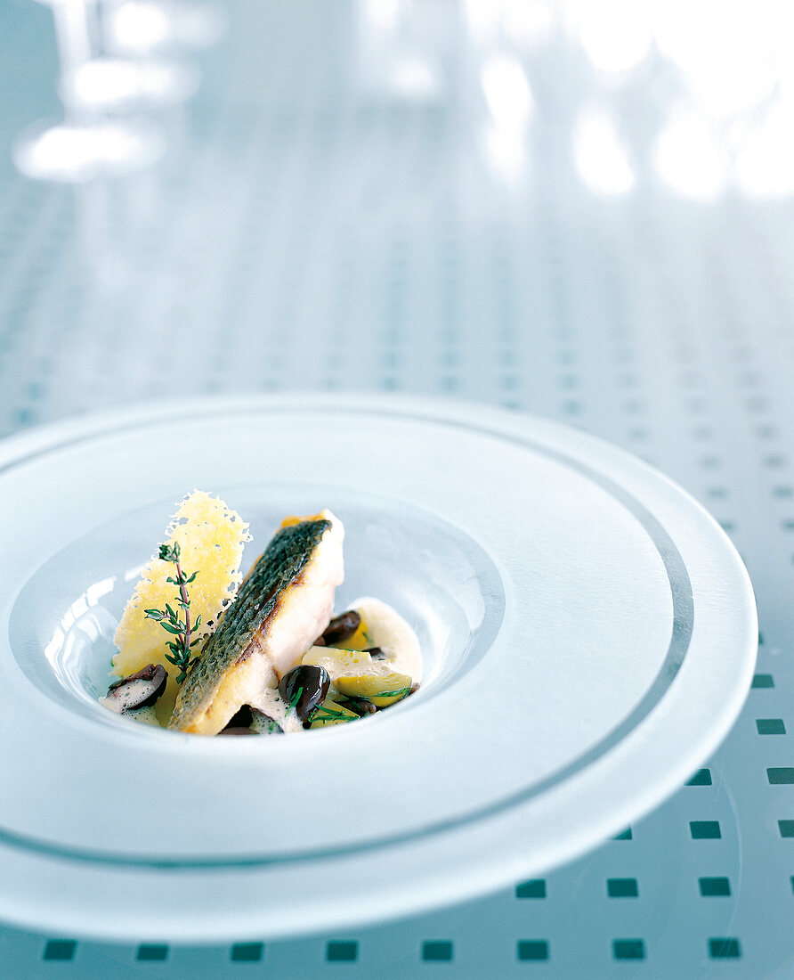 Sea bass with potato, olive and fondue on plate