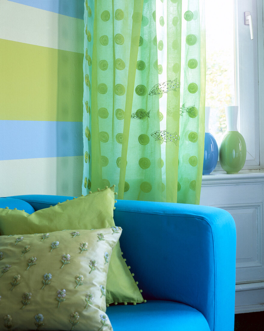 Blue sofa with green pillows in front of organza green curtain
