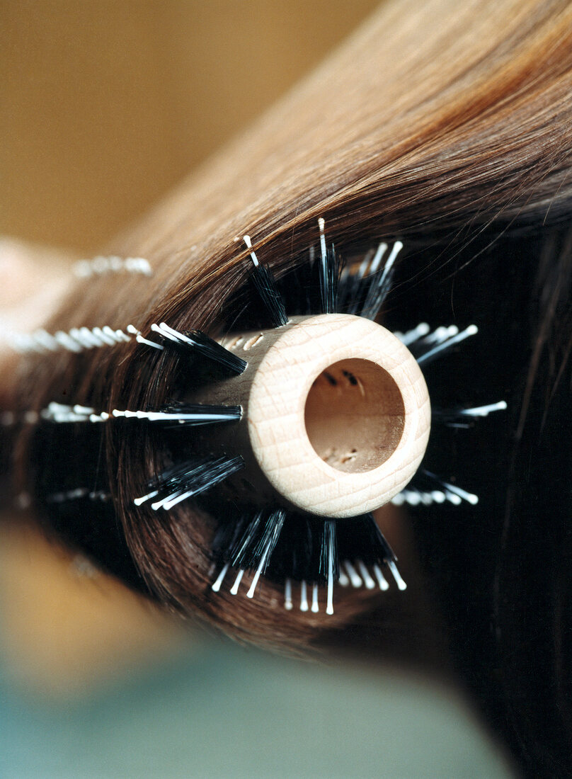 Extreme close-up of woman with dark hair combing hair with round brush