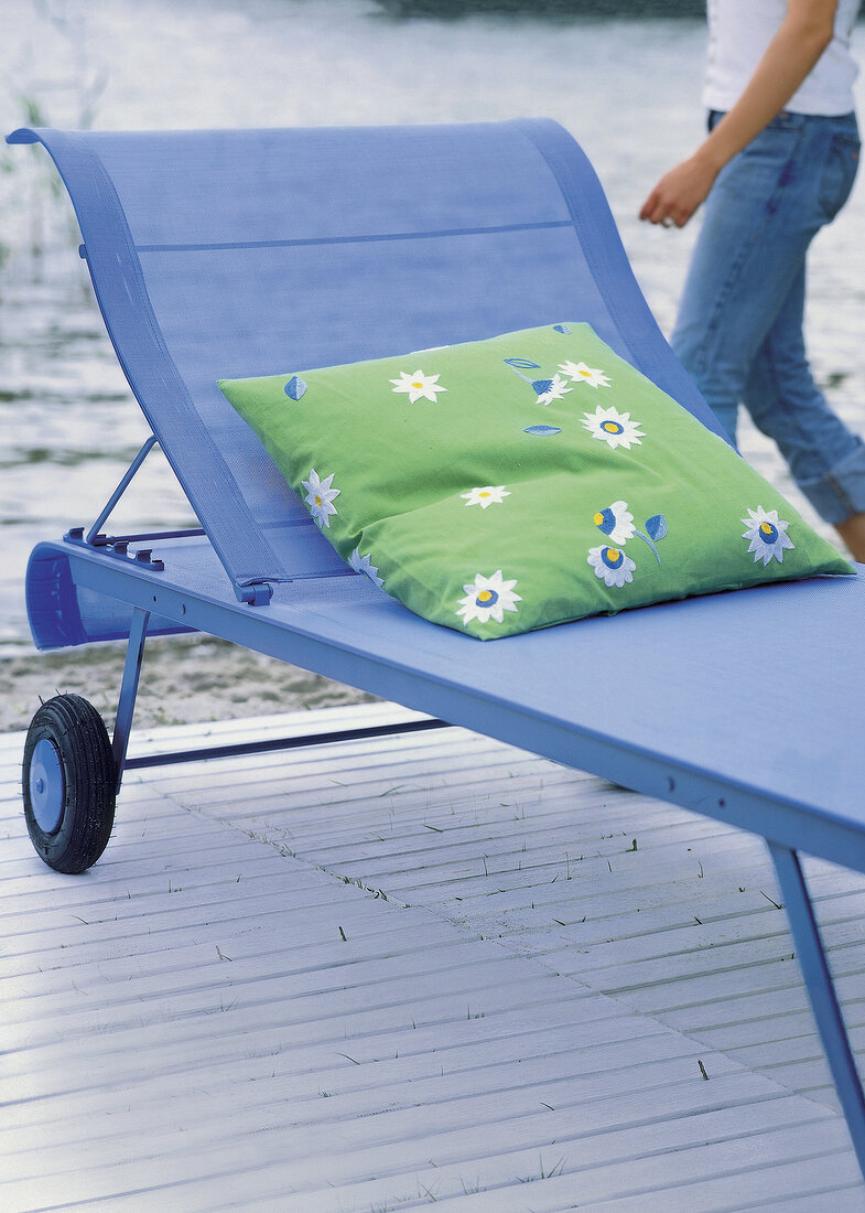 Green floral pattern cushion on blue sun lounger with wheels on wooden pier