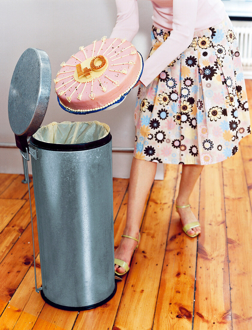 Low section of woman throwing 40th birthday cake in trash, milestone