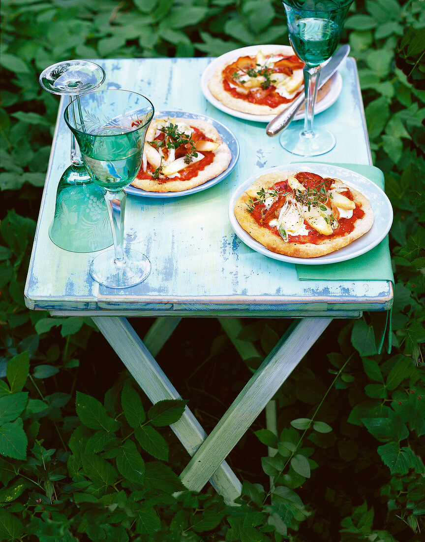 Asparagus pizza with leek and ham on table set outdoors