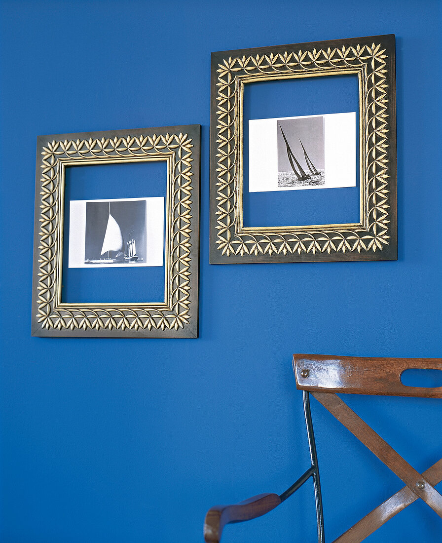 Two black picture frame with gold ornament hanging on blue wall