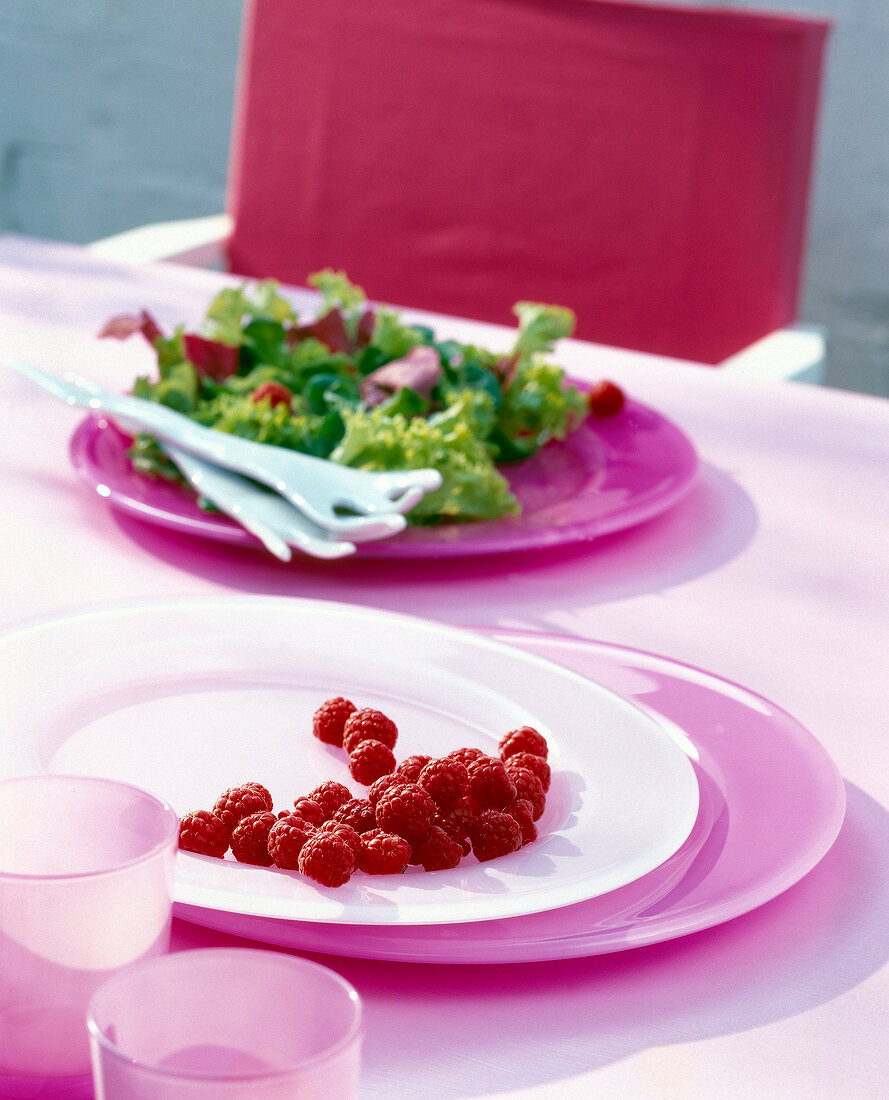 Glass plate with raspberries and salad in background
