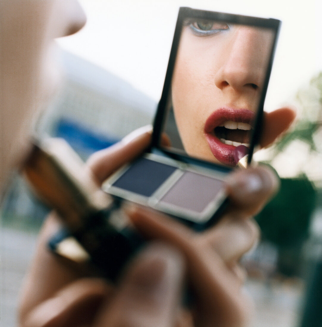 Frau schaut in Spiegel und trägt Lippenstift auf