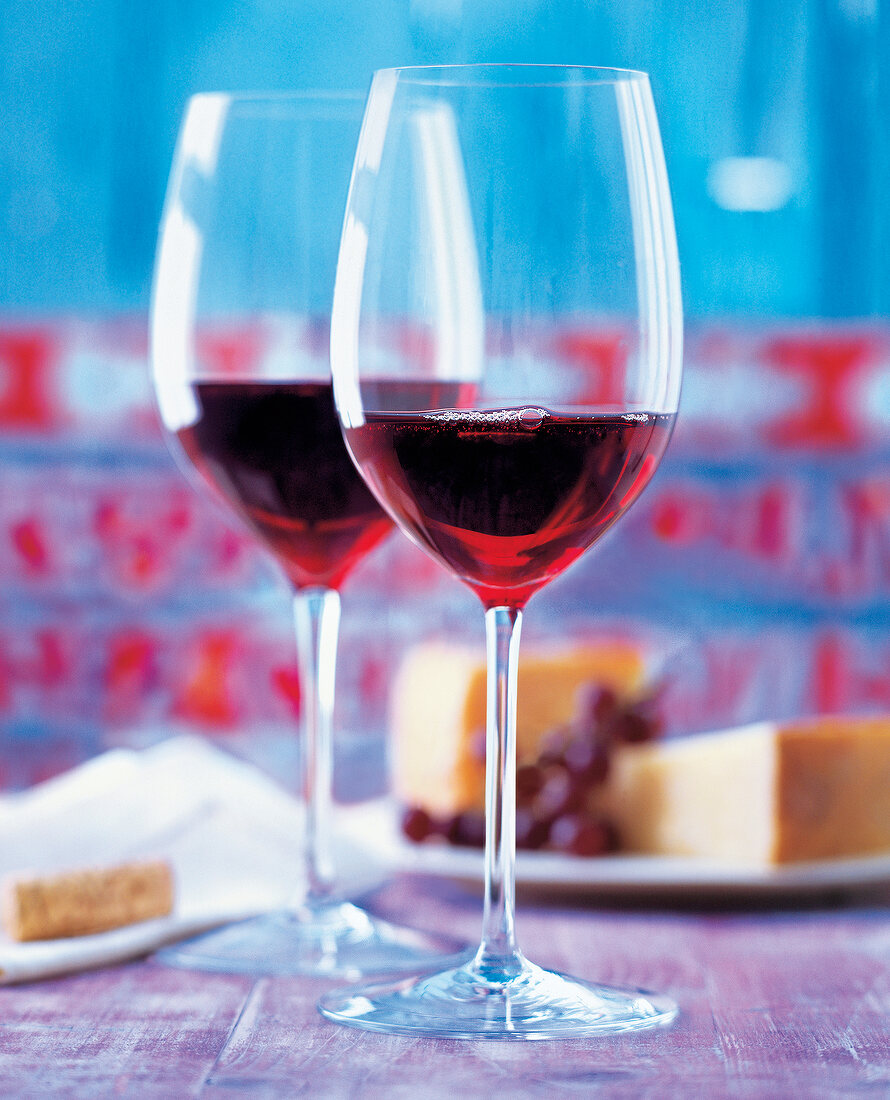 Two glasses with red wine in front of plate with cheese