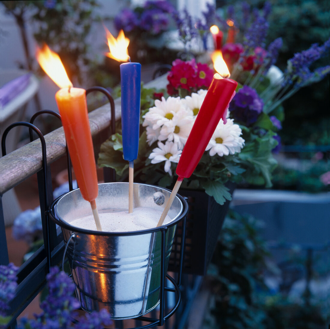 Lit wax torches with wooden handle in garden at evening with flowers in background