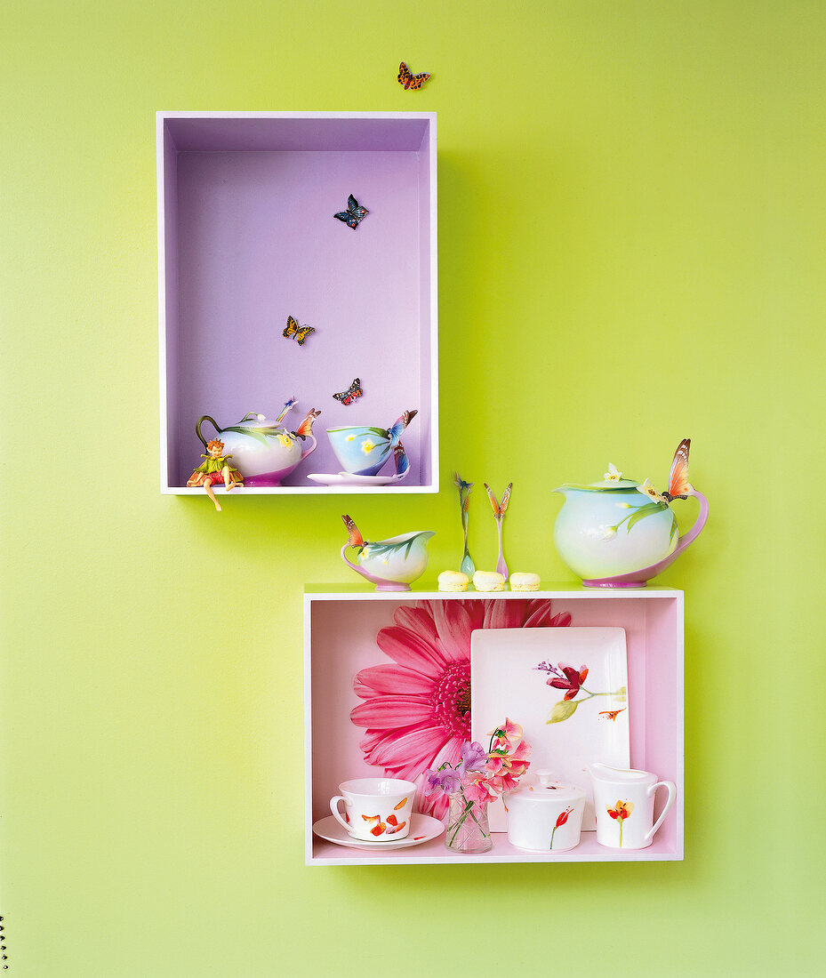 Two display cabinets with flower printed crockery on green wall
